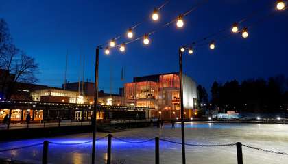Edessä pimeässä valaistu jääkenttä ja matala rakennus. Takana Espoon kulttuurikeskus, joka on valaistu oranssilla värillä.
