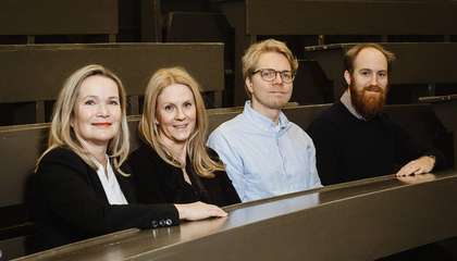 Neljä ihmistä istuu vierekkäin auditoriossa.